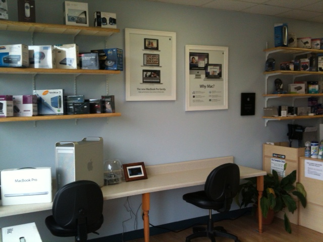 photo of a desk with a mac on it and shelves with computer parts. There's a poster saying "Why Mac?" and bullet points on it