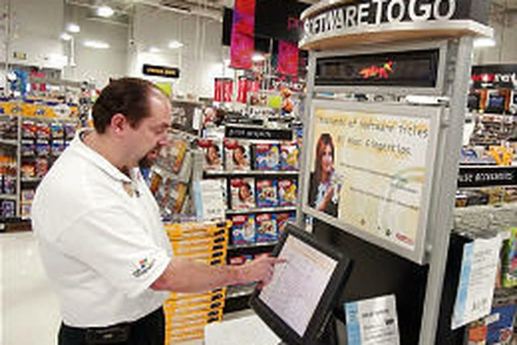 a man pointing at a kiosk in a compusa store