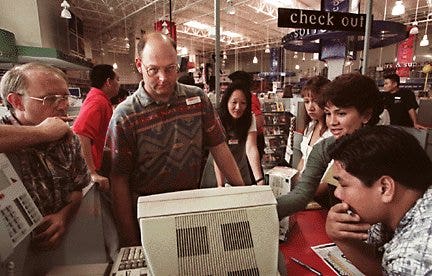 a group of people huddled around a desktop computer in CompUSA