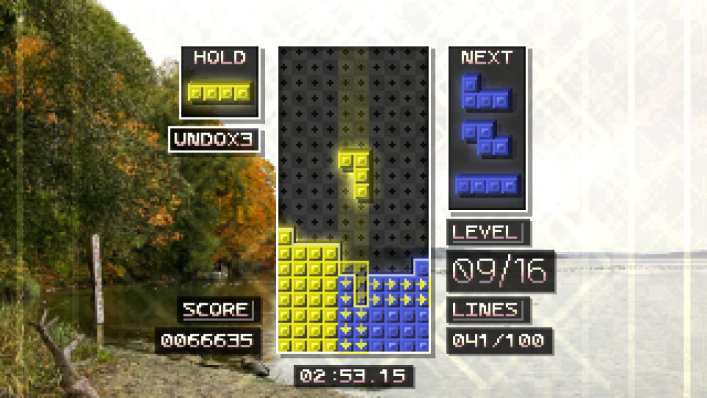 falling blocks in a Tetris screen, in front of a low res photo of a lake shore